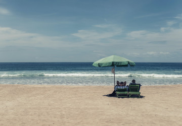 2 people sitting beach chairs under an umbrella on the beach